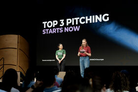 Two speakers on stage launching a Top 3 pitching session before an audience
