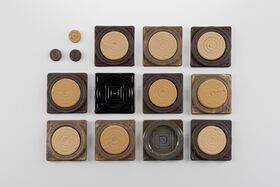 Top view of small round and square brown tiles with spiral patterns arranged in a neat grid on white.