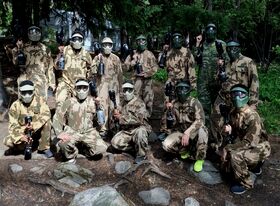 Group of people in camouflage overalls with paintball guns posing in a forest clearing
