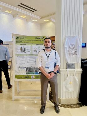 Person in smart casual clothes stands by a textile research poster and white printed T-shirt at a conference.