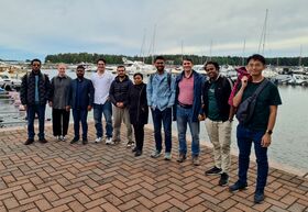 Group of people posing on a harbourside promenade, yachts and forested shoreline in the background