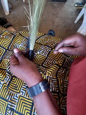 Hands tying a grass broom handle over a yellow and black patterned fabric skirt.