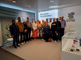 Mixed group of people posing in an office lobby with UPM logo and text ‘We renew the everyday’ on the wall