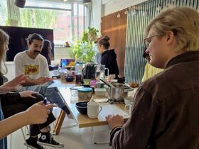 Group of young adults sitting around a table cooking and talking in a bright, plant‑filled room