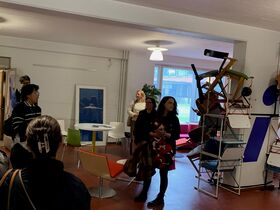 People touring a modern room with stacked chairs, colourful furniture and wall art