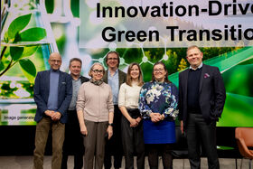 Seitsemän aikuista seisoo lavalla vihreän siirtymän innovaatiobannerin edessä