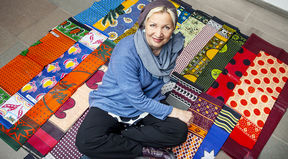 Saija Hollmén istumassa lattialla risti-istunnassa värikkäiden afrikkalaisten kankaiden päällä.