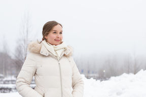 Heli Julkunen seisoo talvisessa maisemassa ja katsoo hymyillen pois kamerasta. Hänellä on päällään valkoinen talvitakki ja taustalla näkyy sumua, puita ja lumihankia.