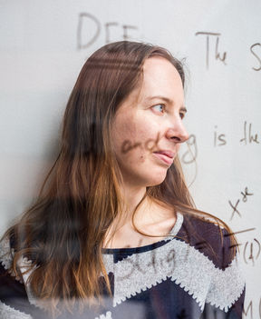 Kaie Kubjas katsoo lähikuvassa sivulle, hänet on kuvattu lasiseinän läpi, jolloin seinälle kirjoitetut matemaattiset kaavat heijastuvat hänen ylleen.