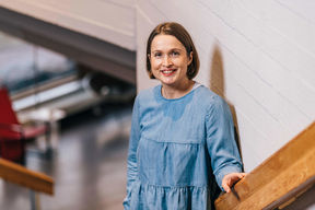 Professori Paula Jouhten nojaa kaiteeseen ja hymyilee kameralle.