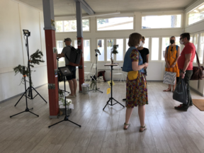 INUSE Research group exhibition space in a bright room with lighting tripods set up, some green branches and 5 people viewing.