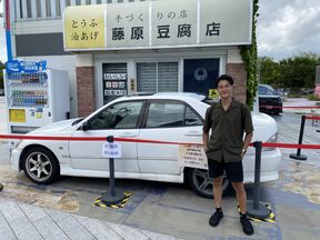 Songwen He seisoo valkoisen auton edessä Hongkongin kadulla. Taustalla kylttejä ja mainostekstejä kantoninkiinaksi.