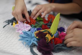 Lähikuva käsistä, jotka kiinnittävät kankaasta tehtyjä kukkia kanaverkkoon