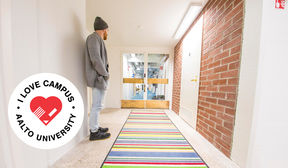 Leigh Ewin stands by the wall on the left, gazing away from camera and towards the doors that are in the centre of the image. I love campus logo in the lower left corner.