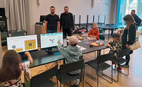 A group of people including children sitting around desks with monitors