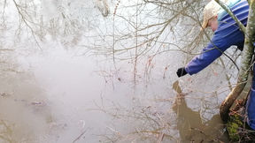 Joen pinta jäätyy, puut heijastuvat veteen. Henkilö kurottaa vedenpintaan.
