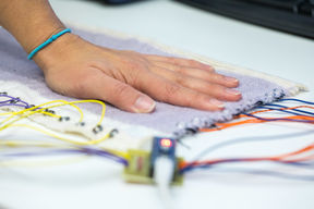 Käsi koskettaa vuorovaikutteista painallusta tunnistavaa kudottua kangasta.