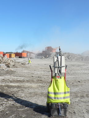 Kuvassa on avolouhos, jossa taustalla monivaiheinen murskauslaitos, joka on toiminnassa. Etualalla tutkimuksessa käytetty mittauslaitteisto (nefelometri).