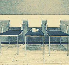 Kolme tyhjää sairaalan odotushuoneen tuolia, joista keskimmäisellä on käytetty kasvomaski