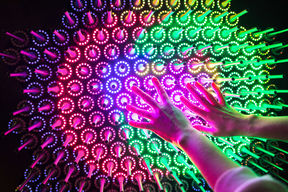 Taideteos, jossa on kirkkaan pinkkejä ja vihreitä valoja. Ihminen koskee teosta keskeltä käsillään.