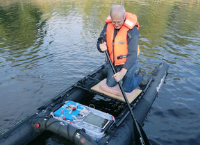 Kuva esittää maaperätutkan toiminnan testausta mittaamalla järvessä, jolloin järven syvyys näkyy ja samalla näkyy pohjan alla olevia maakerroksia mittausprofiilissa. Väitöstukimuksen yhteydessä rakennettu maaperätutka on lautan keskiosassa olevassa muovilaatikossa. Kuvassa on väitöskirjan kirjoittaja Veli Voipio. 