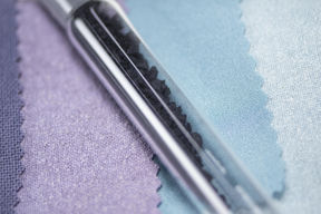 A close-up of a glass tube with black particles, lying on pastel fabric swatches in shades of purple and blue.