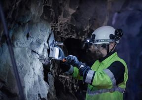 Henkilö työvaatteissa ja kypärässä työskentelee luolassa kiviseinällä työkaluilla.