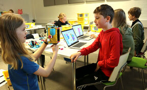 Lapset luokkahuoneessa harjoittelevat robotiikkaa kannettavilla tietokoneilla ja LEGO-roboteilla.