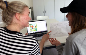 Kaksi tyttöä istuu tietokoneen ääressä tarkastelemassa paperille tehtyä kaaviota.