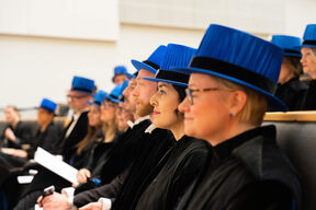 People wearing blue academic hats and black gowns seated in rows during a ceremony.
