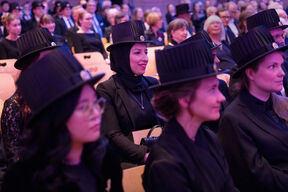 People wearing academic dress and traditional black hats, seated in rows at a formal event.