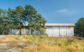 Modern storage building with grey facade with wooden details and windows surrounded by trees and grass under a clear blue sky.