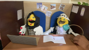 Kaksi nukkea istuu työpöydän toimistolavasteessa: musliminainen hijabissa kannettavan tietokoneen edessä ja juutalainen mies kipa päässään.