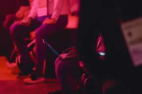 People sitting with laptops and mobile phones in a dimly lit, red-tinged room.