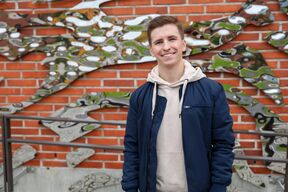 Oskari Heikkilä tiilirakennuksen seinällä olevan metallisen taideteoksen edessä