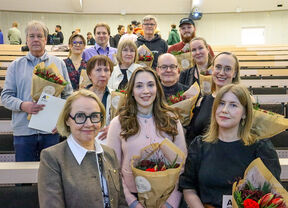 A group of people standing in a lecture hall holding bouquets of flowers and certificates.