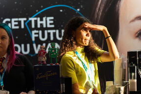 Two women at a booth with robot toys and a box of Karl Fazer chocolates. A sign reads 'Get the future you want'.