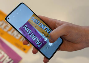 A hand holding a smartphone, capturing a photo of two Talent Expo flyers in purple and yellow.