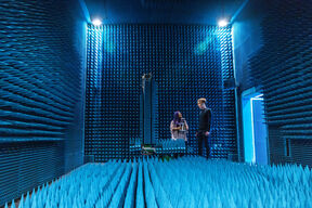 Two people stand in a room with blue, spiked walls and floor, likely an anechoic chamber used for testing acoustics.