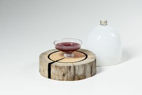 A glass bowl with red liquid on a wooden slab, next to a white dome-shaped object.