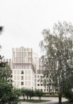 Modern multi-storey building with large windows, surrounded by trees and greenery.