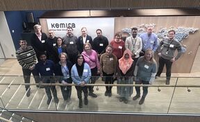 A group of people standing in front of a Kemira sign and a world map made of small spheres.