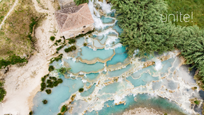 Aerial view of turquoise terraced pools, rocky banks, trees and a small tiled-roof house, with the word “unite!”