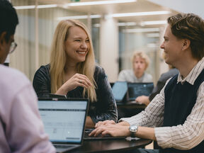 Opiskelijaryhmä juttelee ja työskentelee kannettavilla kirkkaassa toimistotilassa