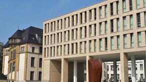 Vanha vaalea rakennus vierekkäin modernin beigen toimistotalon ja ruosteenruskean veistoksen kanssa