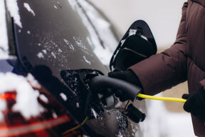 Person in winter coat charges a snowy electric car