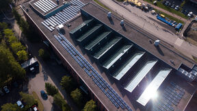 Aerial view of large flat-roof building with glass skylights, solar panels and nearby road with parked vehicles