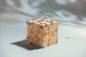 Puisesta kuutiosta tehty lamppu, hopeiset metallikuviot ja uria pitkin hehkuva lämmin oranssi valo