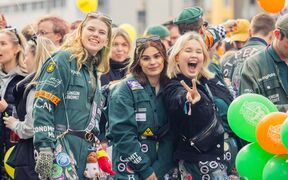 Studenter i gröna overaller på ett livligt utomhusevenemang, ballonger och en gör fredstecken