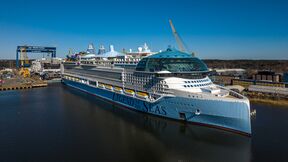 Large white cruise ship named Legend of the Seas docked at an industrial shipyard under a clear blue sky.